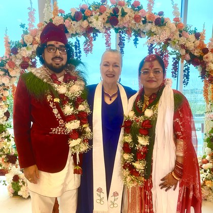 Sarah with a couple beneath a floral arch during their traditional Indian wedding ceremony